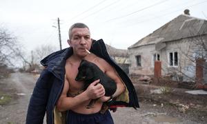 A man holds a dog as he walks past a damaged house following shelling in Mariupol, in southeastern Ukraine.