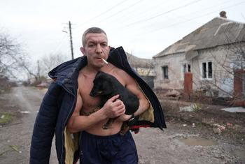 A man holds a dog as he walks past a damaged house following shelling in Mariupol, in southeastern Ukraine.