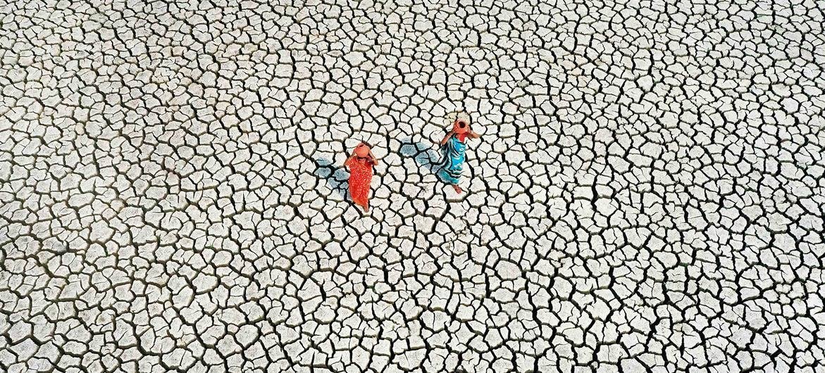 On bone-dry land, severely affected by drought, 2  women hunt  for their regular  h2o  supply.