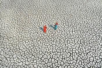 On bone-dry land, severely affected by drought, two women search for their daily water supply.