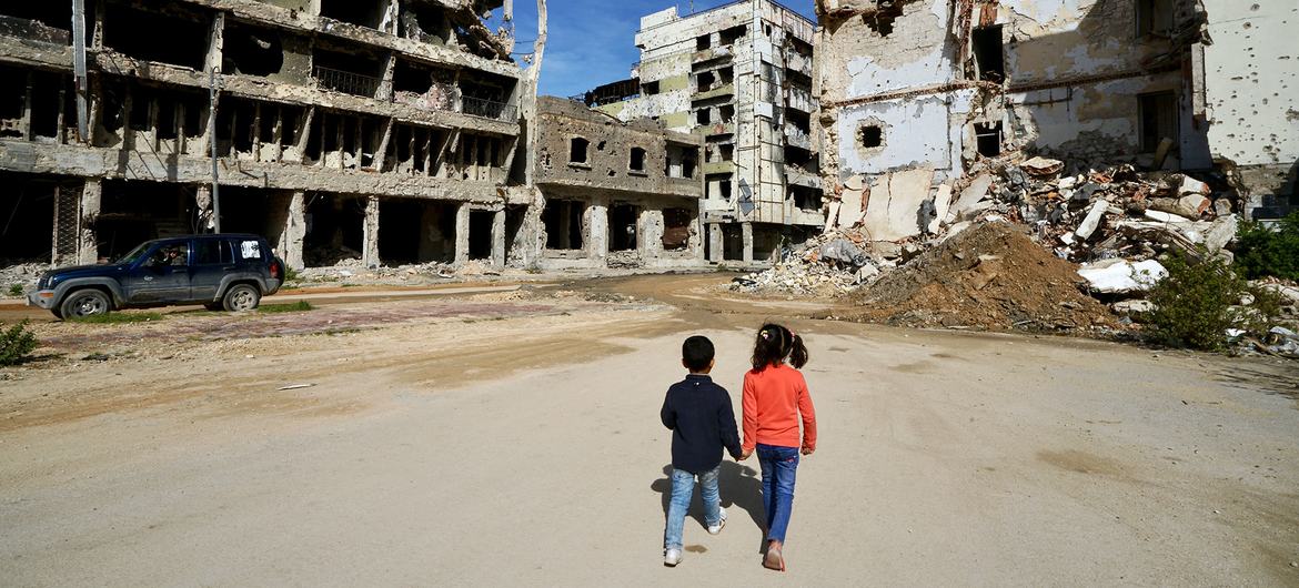Anak-anak berjalan melewati bangunan yang rusak di Benghazi di Libya.