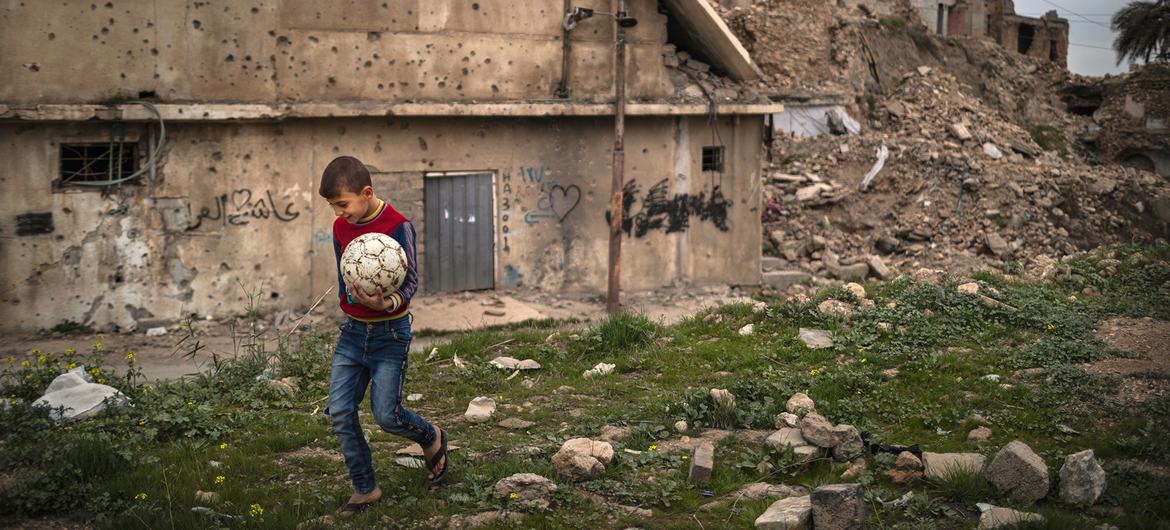 Menino carrega uma bola de futebol na Cidade Velha de Mossul, no Iraque