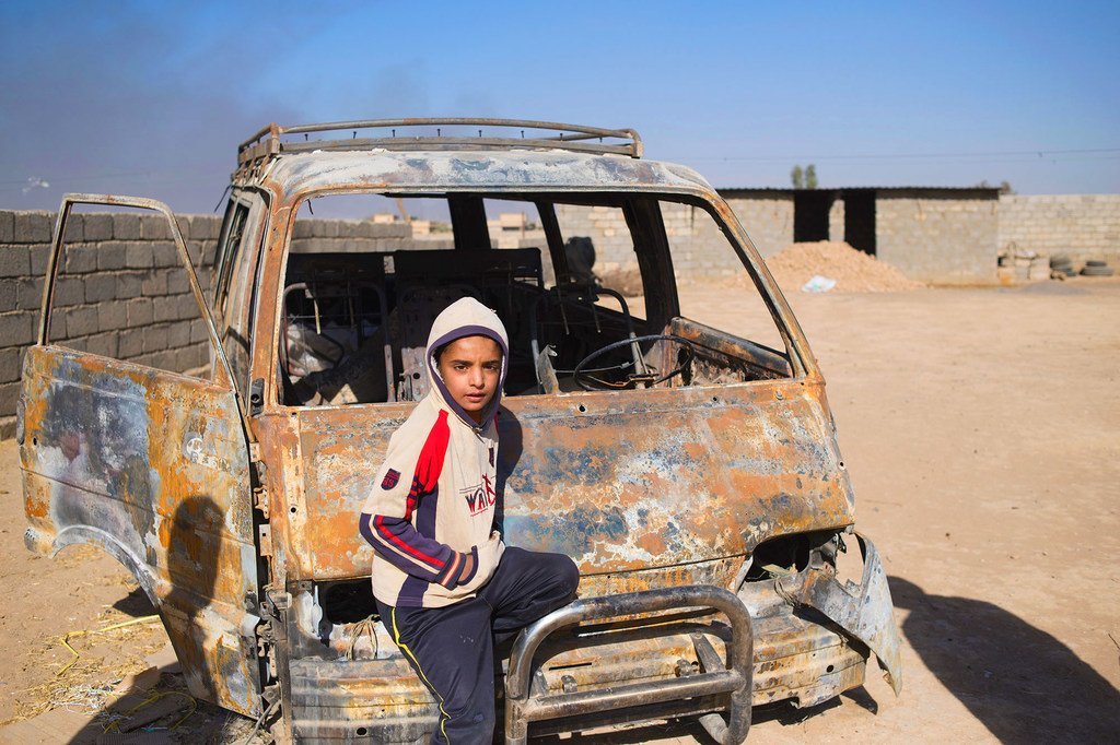 伊拉克一名小男孩站在一辆被伊黎伊斯兰国烧毁的汽车旁边。（资料图片）