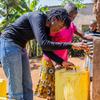 Balozi wa Nia Njema UNICEF Vanessa Nakate akimsaidia mtoto kujaza kopo la manjano na maji kutoka kwenye kituo cha maji kinachotumia nishati ya jua nchini Rwanda.