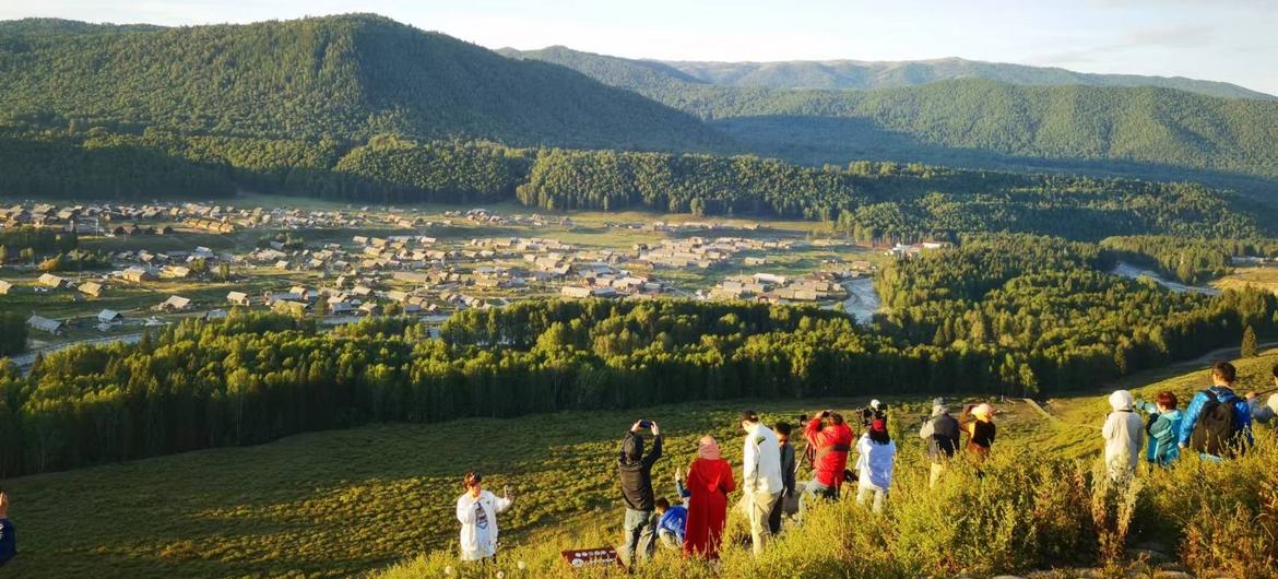 新疆喀纳斯，游客们在山坡上俯瞰一个村庄美丽的景色。