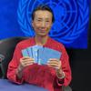 联合国秘书长卢伟在新闻发布会上举起她的证件，背景是联合国徽标。