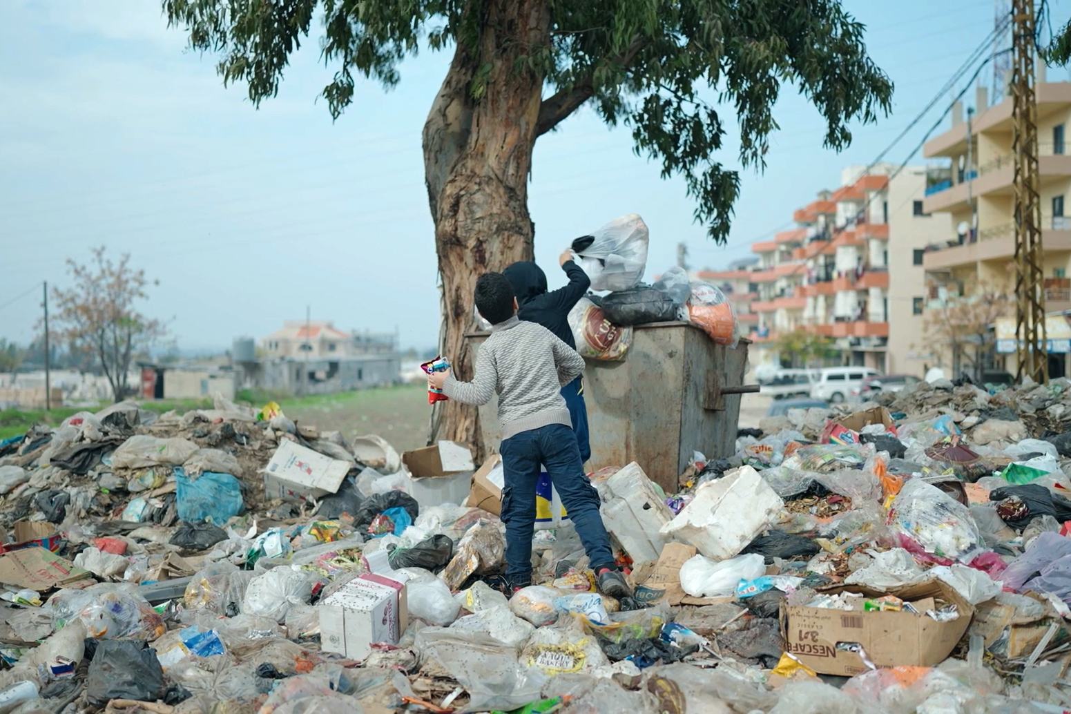 أطفال يرمون القمامة في الحاوية الممتلئة بأكياس القمامة.