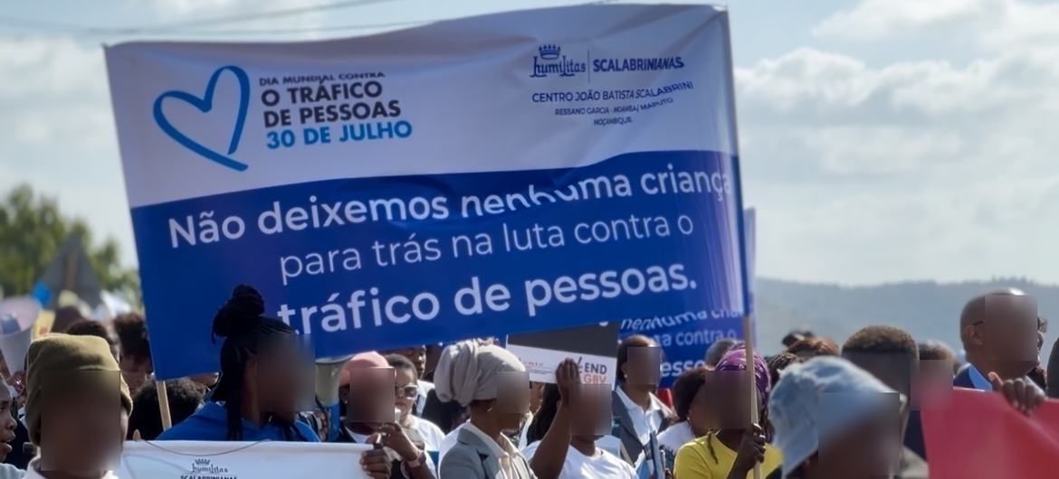 Uma multidão participa de uma manifestação pública segurando uma faixa sobre o Dia Mundial de Combate ao Tráfico de Pessoas em Moçambique.