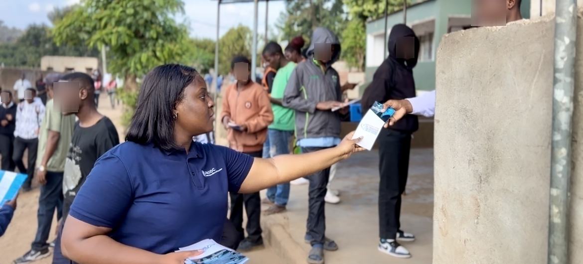 Um funcionário do Unodc distribui materiais para uma fila de pessoas em um local ao ar livre em Moçambique.