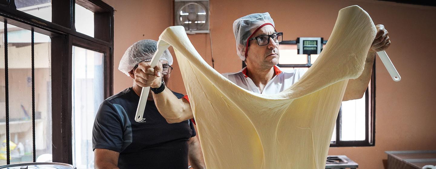 Guillermo desmenuza con su mano un queso mozzarella fresco para mostrar el proceso de producción artesanal que implica la elaboración de este tipo de queso.