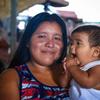 Una madre refugiada indígena venezolana sostiene a su bebé. El bebé se lleva la mano a la boca.