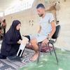 Ibrahim Abdel Nabi, un palestino desplazado en Gaza, sentado en una silla mientras su esposa le ayuda a ponerse la prótesis hecha a mano.