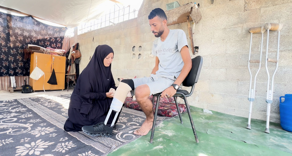 Ibrahim Abdel Nabi, un Palestinien déplacé à Gaza, assis sur une chaise tandis que sa femme l'aide à ajuster la prothèse faite main.