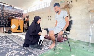 Ibrahim Abdel Nabi, un palestino desplazado en Gaza, sentado en una silla mientras su esposa le ayuda a ponerse la prótesis hecha a mano.