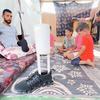 إبراهيم عبد النبي، النازح الفلسطيني في غزة، يجلس مع أبنائه وهو ينظر إلى الطرف الاصطناعي الذي صنعه ليعوضه فقدان إحدى قدميه.