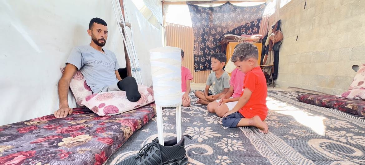 إبراهيم عبد النبي، النازح الفلسطيني في غزة، يجلس مع أبنائه وهو ينظر إلى الطرف الاصطناعي الذي صنعه ليعوضه فقدان إحدى قدميه.