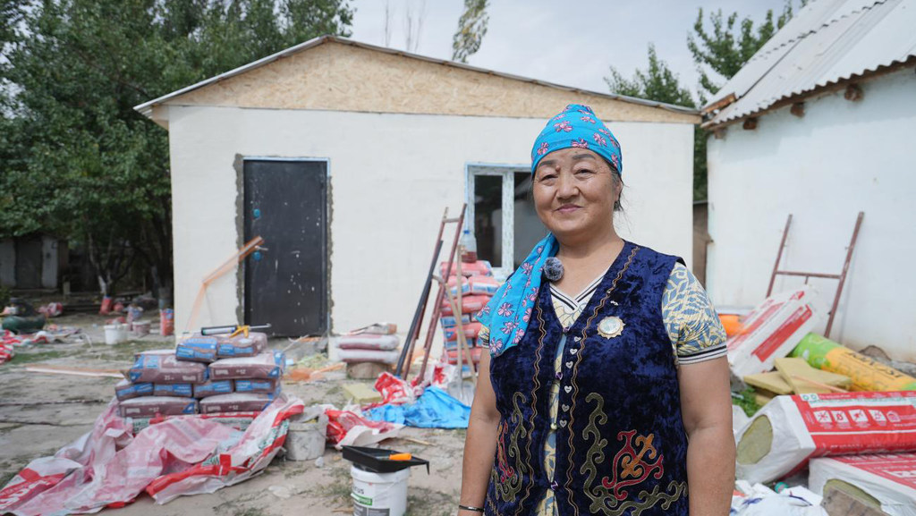 Киргизская женщина стоит перед строящимся новым домом, окруженная строительными материалами.