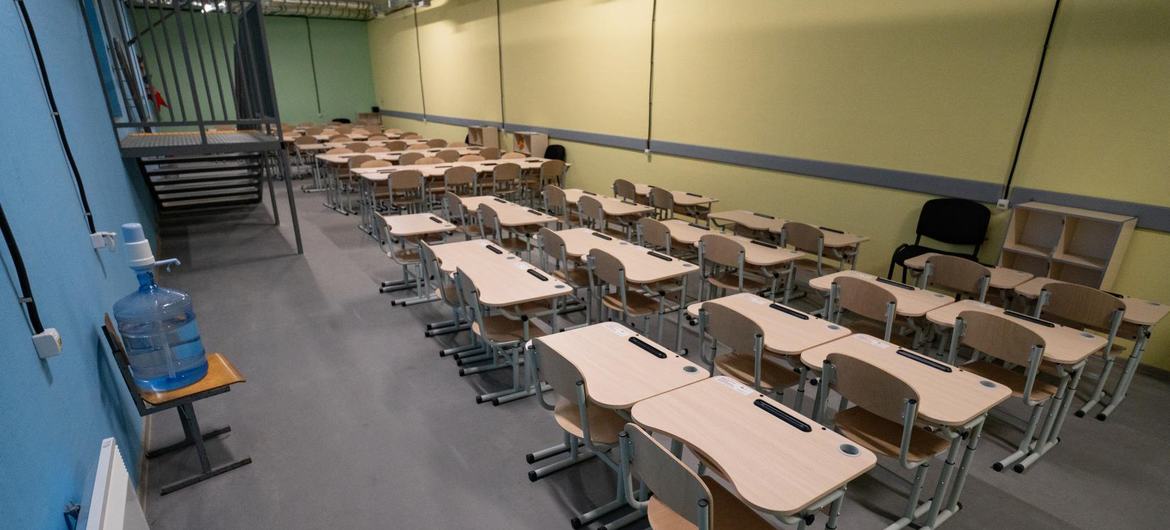 Fileiras de carteiras e cadeiras vazias em uma sala de aula improvisada dentro de um abrigo na Ucrânia.