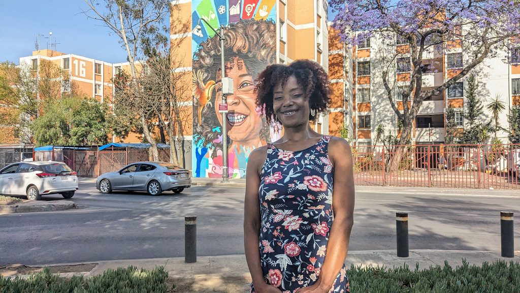 Kathleen Murrain retratada frente a un mural con los Objetivos de Desarrollo Sostenible de la ONU y una niña afrodescendiente, en la Alcaldía de Iztapalapa, en la Ciudad de México.