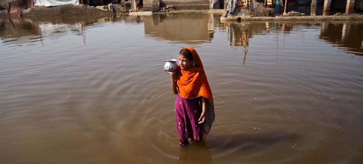 पाकिस्तान में बाढ़ के पानी से गुज़रती एक युवती.