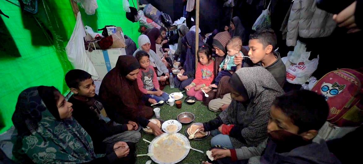 عائلة حول أطباق بسيطة وقت الإفطار في رمضان، في خيمة إيواء مؤقتة في مدينة دير البلح، وسط غزة.