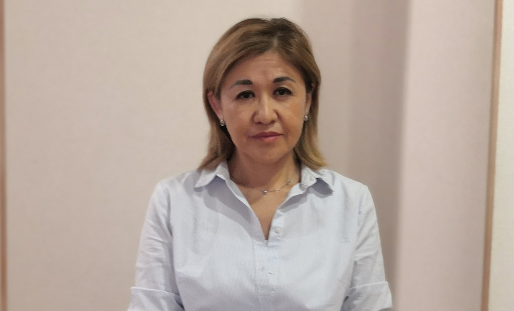 Казахстанская женщина в светло-голубой рубашке позирует для портрета в помещении.