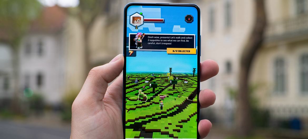 A young person holds a cell phone with the game Minecraft Earth.
