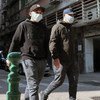 Dois homens usando máscaras faciais caminham por uma rua em Macau.