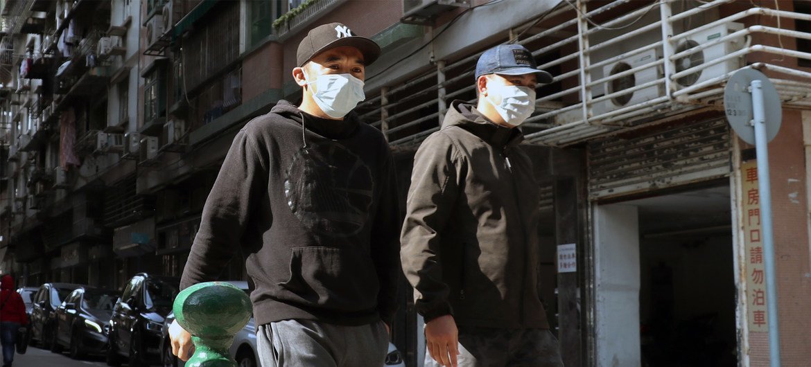 Dois homens usando máscaras faciais caminham por uma rua em Macau.