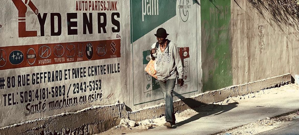 A man walks along a street in Delmas, Port au Prince, Haiti, past a concrete wall with advertisements for auto parts and Pam.