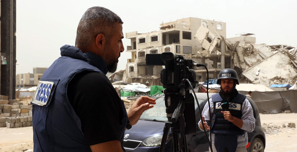 يعمل المصور الصحفي سامي شحادة مع زميل له في أحد شوارع مدينة غزة، ويظهر في الخلفية مبنى متضرر.