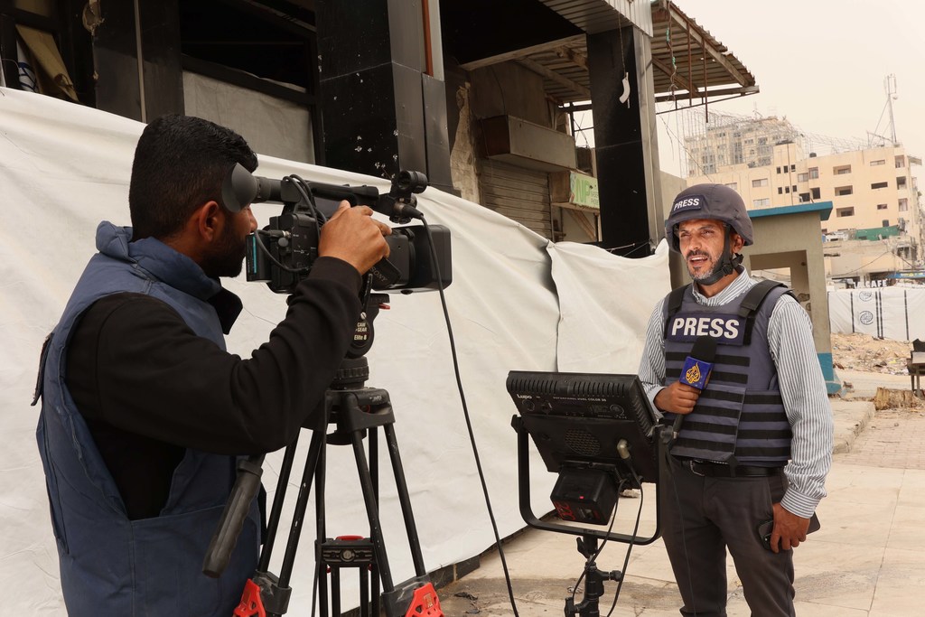 Un periodista palestino, Moamen Al-Sharafi, con casco y chaleco de prensa, está siendo filmado por un equipo de cámaras en Gaza.