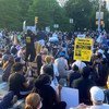 Una gran multitud de personas se sienta en una calle de Brooklyn, Nueva York, durante una protesta. Un cartel en primer plano dice: "¡Justicia para Tony McDade, las vidas de las personas trans negras importan!".