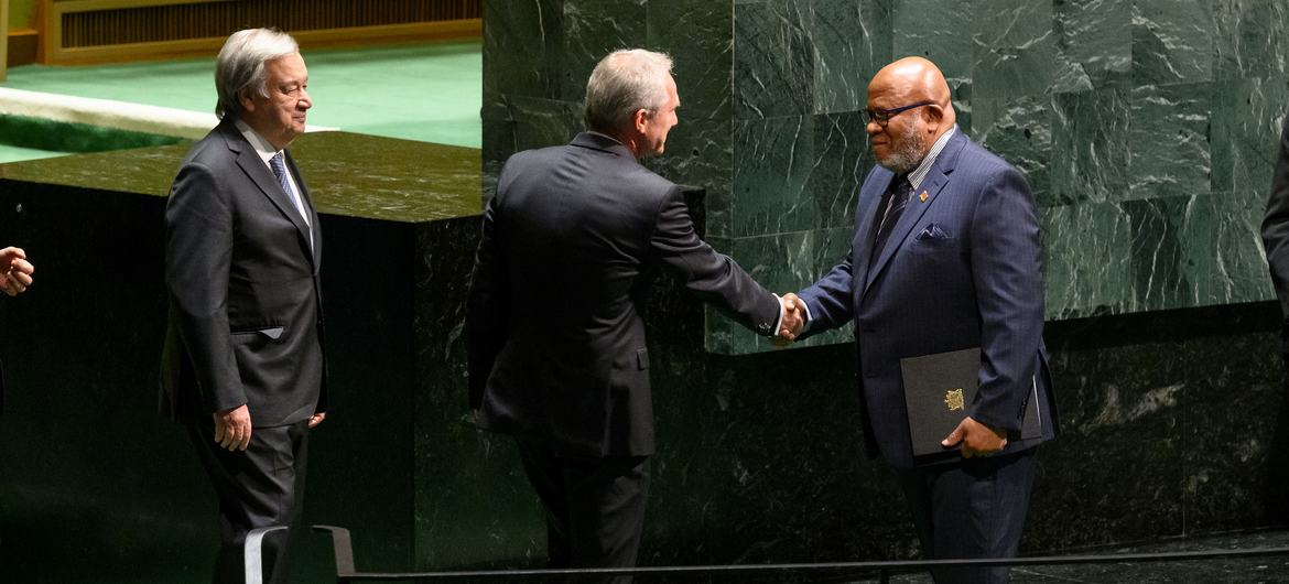 Presidente da Assembleia Geral, Csaba Kőrösi (centro), cumprimenta o Embaixador Dennis Francis de Trinidad e Tobago, Presidente eleito da 78ª sessão da Assembleia Geral da ONU. O secretário-geral António Guterres observa (à esquerda).