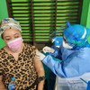 В Индонезии беженка получает вакцину от COVID-19 от медицинского работника в средствах индивидуальной защиты.