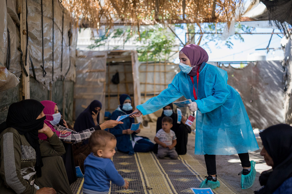 Una trabajadora sanitaria, ataviada con un traje protector, distribuye información a mujeres y niños en un campo de refugiados en el Líbano.