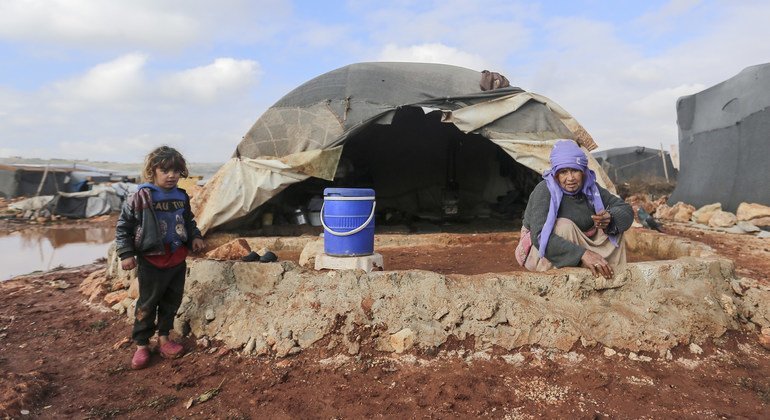 طفل يقف إلى جانب سيّدة تعمل على إقامة حاجز من الطين لمنع مياه الفيضانات من دخول خيمتها في شمال غرب سوريا.