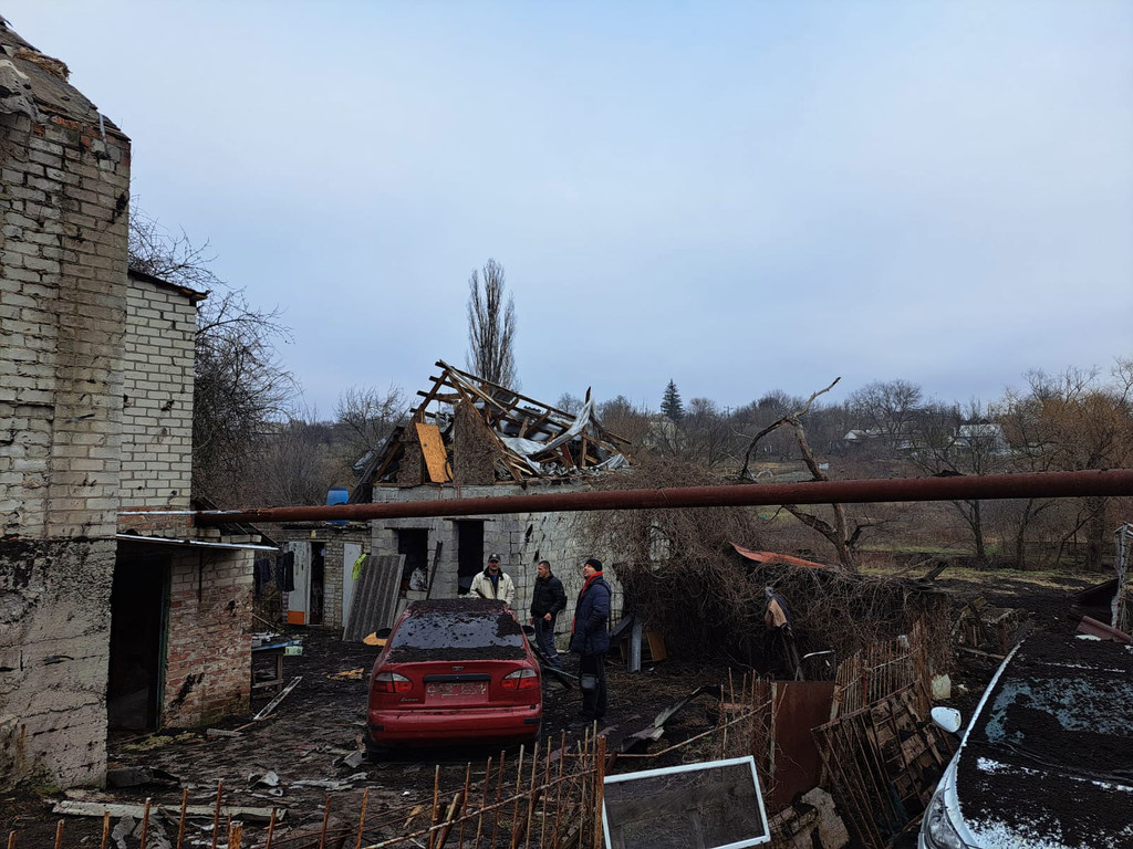 Edificio dañado y escombros en Dnipro, Ucrania, tras los ataques con misiles, con un coche rojo y varios hombres en primer plano.