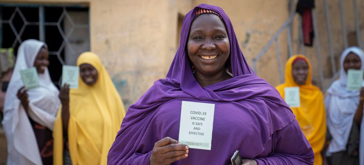 Женщина показывает свою карту вакцинации COVID-19 вместе со своими сестрами в Кано, Нигерия.