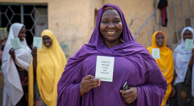 سيدة تبتسم وهي تحمل بطاقة التطعيم ضد كوفيد-19 في نيجيريا.