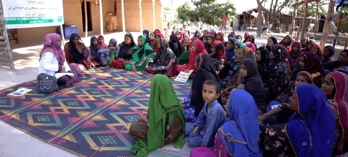 پاکستان کے ایک دیہی گاؤں میں کمیونٹی بیداری کی میٹنگ، خواتین اور ایک نوجوان لڑکی کے ساتھ ایک چٹائی پر بیٹھی اسپیکر سن رہی ہے۔