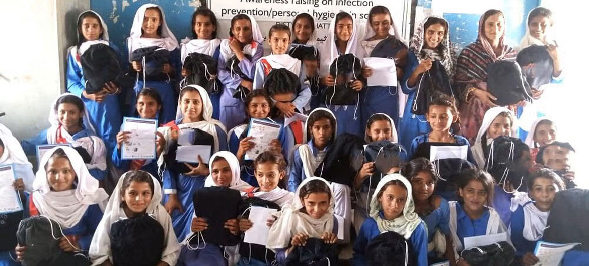پاکستان میں اسکول کی طالبات کا ایک گروپ نیلی یونیفارم اور سفید اسکارف پہنے ہوئے، انفیکشن سے بچاؤ اور ذاتی حفظان صحت سے متعلق آگاہی مہم میں حصہ لے رہا ہے۔ ان کے پاس تعلیمی سامان اور تھیلے ہیں۔