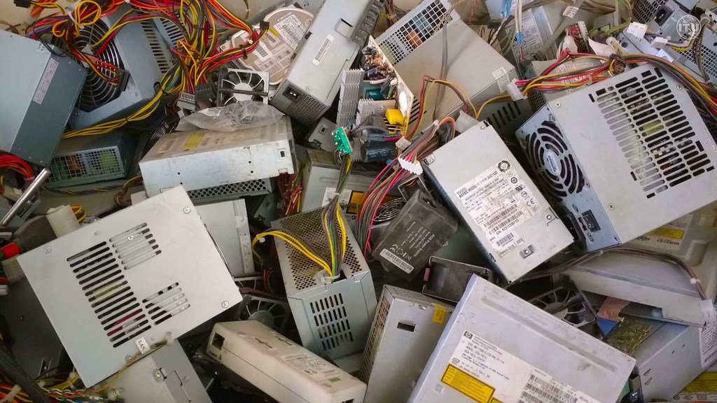 Uma pilha de fontes de alimentação de computador descartadas e cabos eletrônicos emaranhados, representando lixo eletrônico.