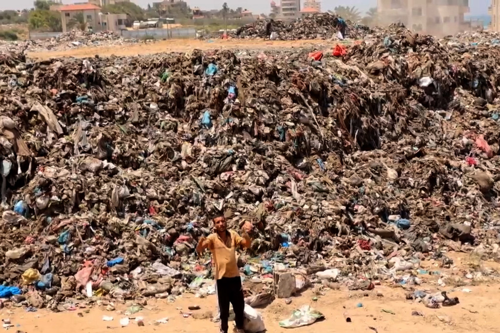 Une personne déplacée à Gaza se tient au milieu d'un tas d'ordures, implorant de l'aide.