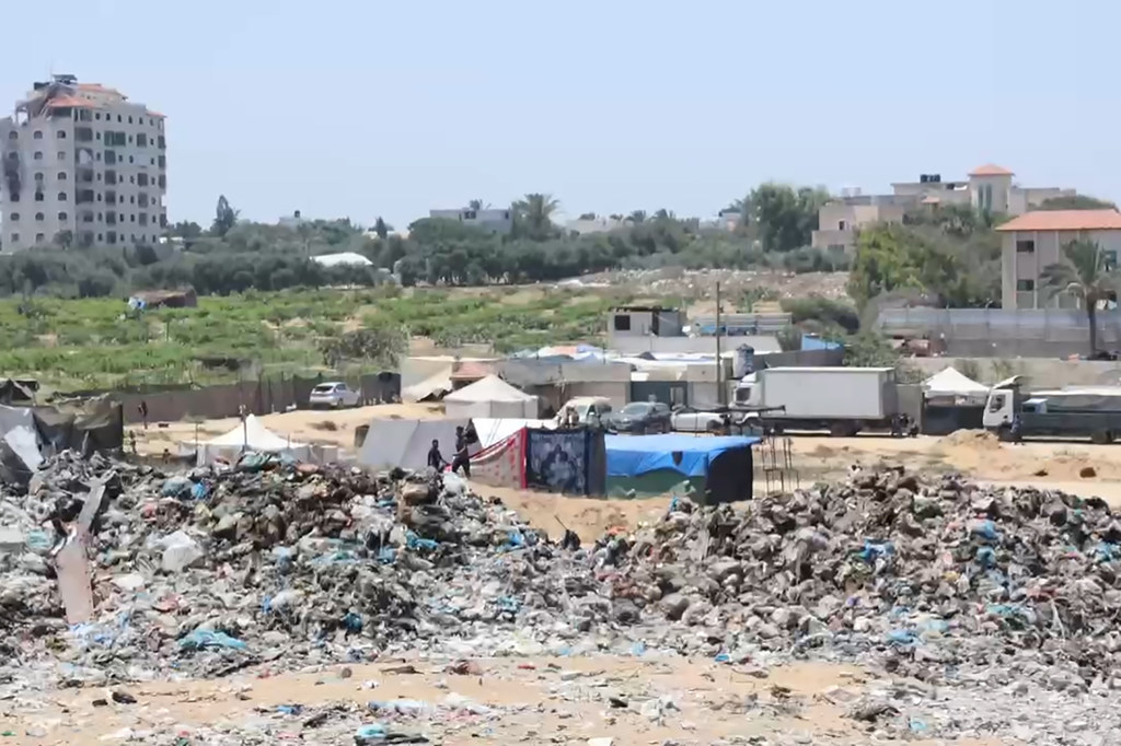 مكب نفايات كبير في مدينة غزة، مع ظهور النازحين وخيامهم في الخلفية.