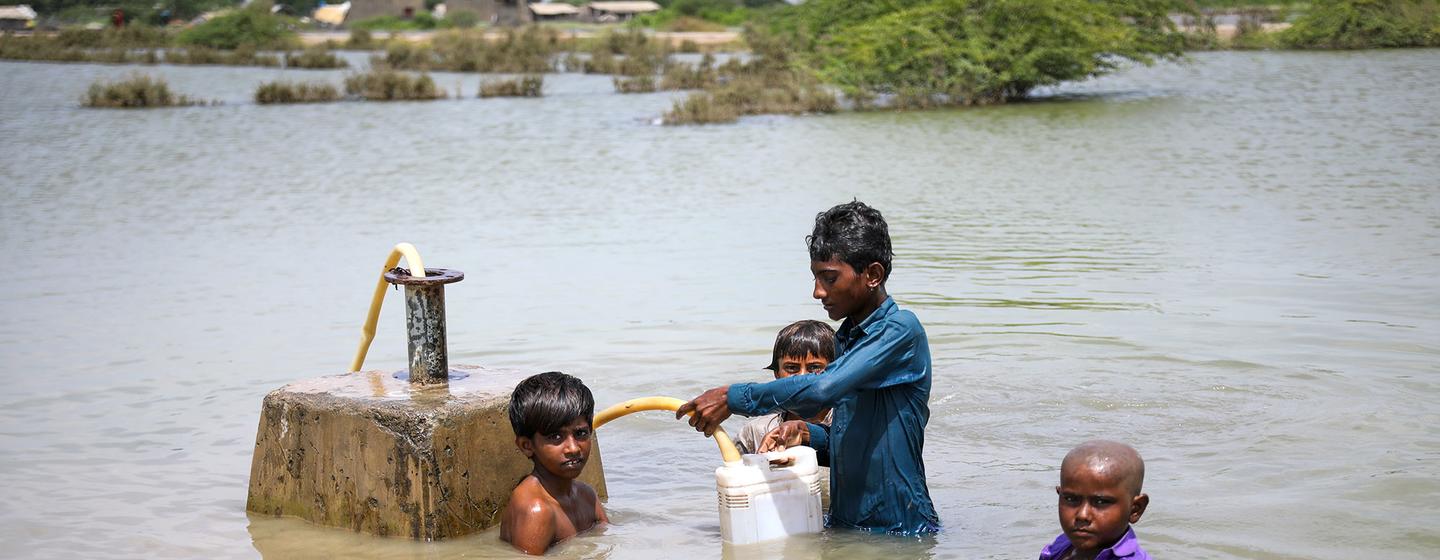 Unos jóvenes recogen agua potable de una línea de suministro de agua bajo el agua de las inundaciones en la provincia de Sindh, Pakistán.