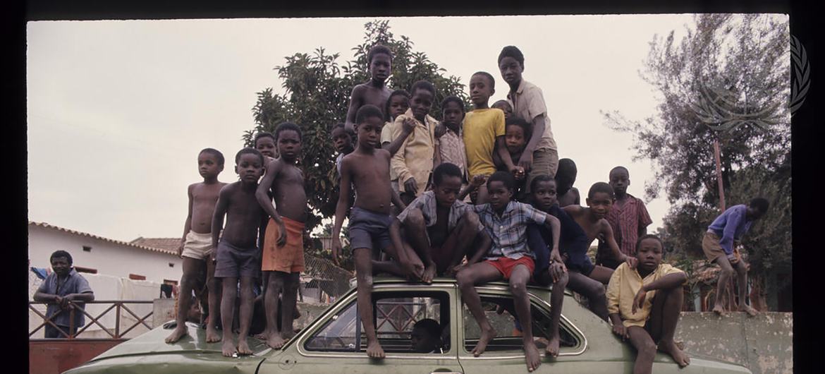 Um grupo de crianças africanas sentadas e em pé sobre um carro verde em um ambiente ao ar livre em Angola.