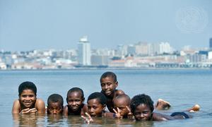 Um grupo de crianças sorridentes na água, com o horizonte da cidade ao fundo.