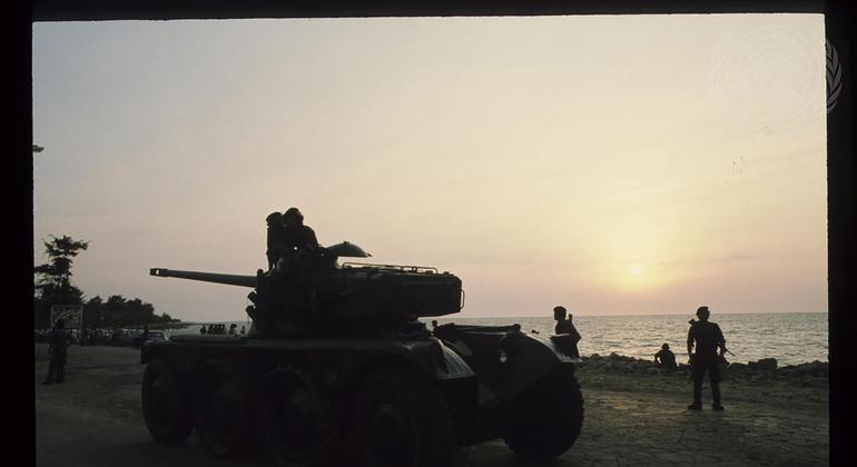 Um veículo blindado militar e soldados são silhuetados contra um pôr do sol sobre o oceano em Angola.
