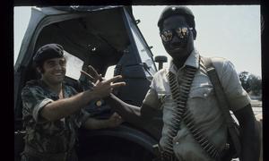 Dois homens em uniformes militares apertam as mãos ao lado de um veículo militar.